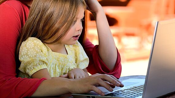 Kind auf Schoß von Mutter vor einem Laptop